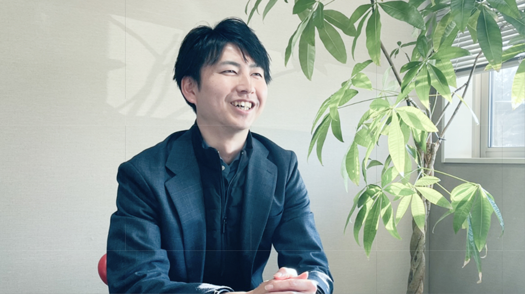 スーツを着た男性が青空を背景にクリップボードを持ちながら微笑んでいる様子。