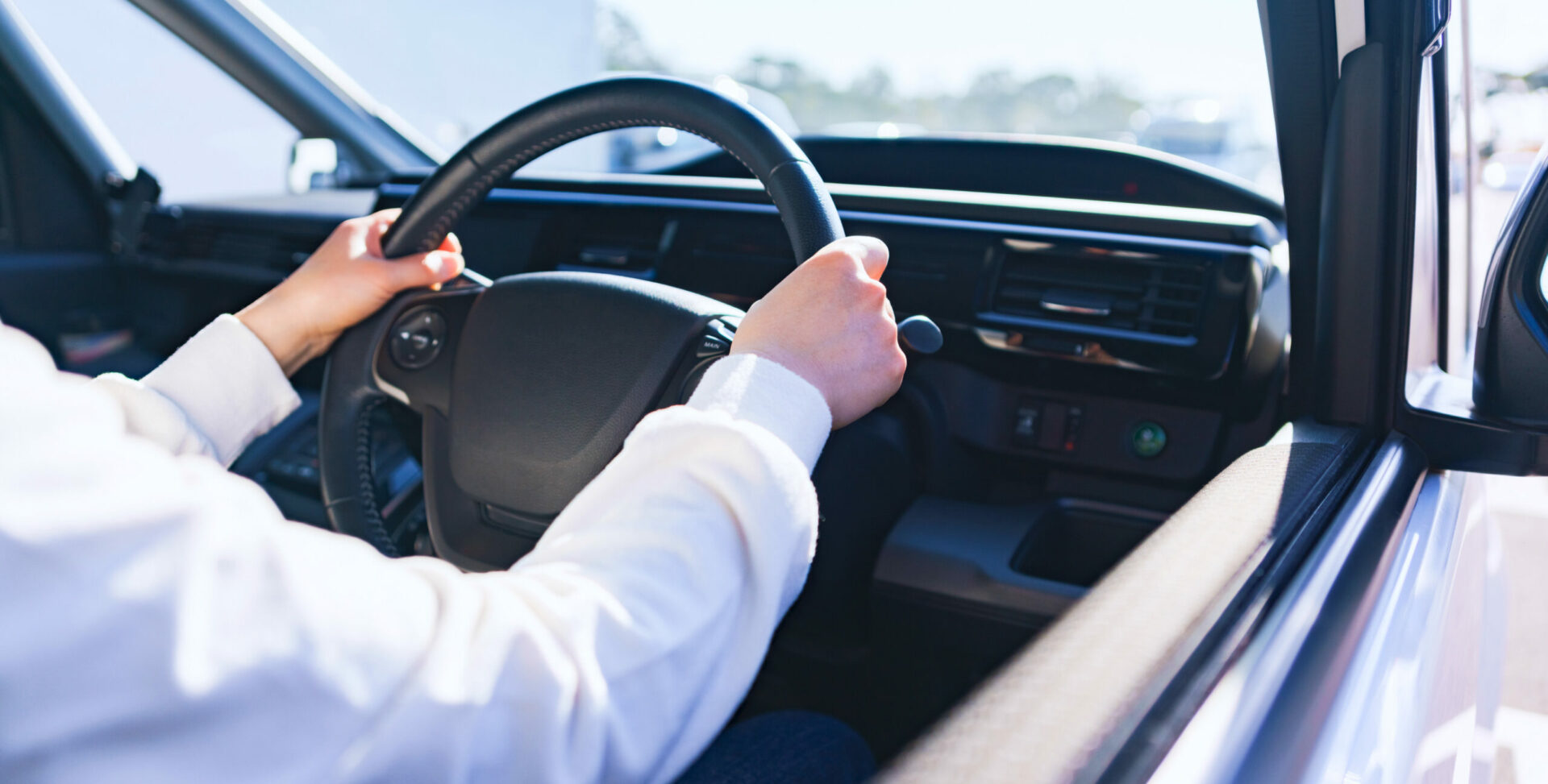 車の運転席に座り、ハンドルを握って運転している人の手元。