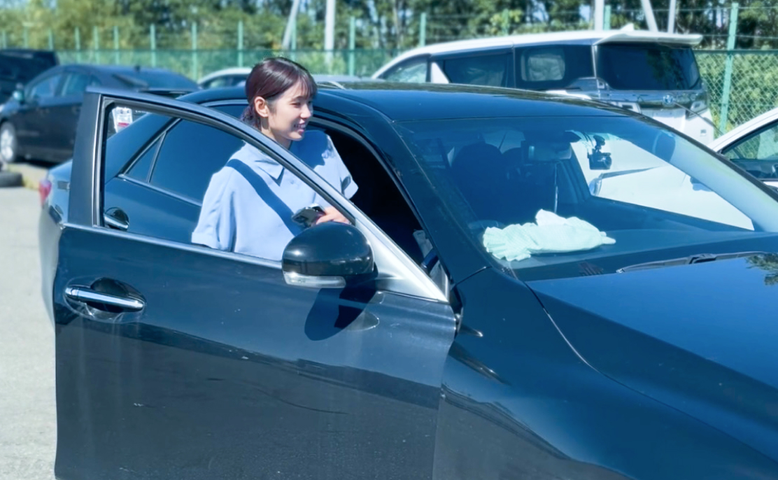 駐車場で黒い車の運転席のドアを開けて乗り込もうとしている女性。